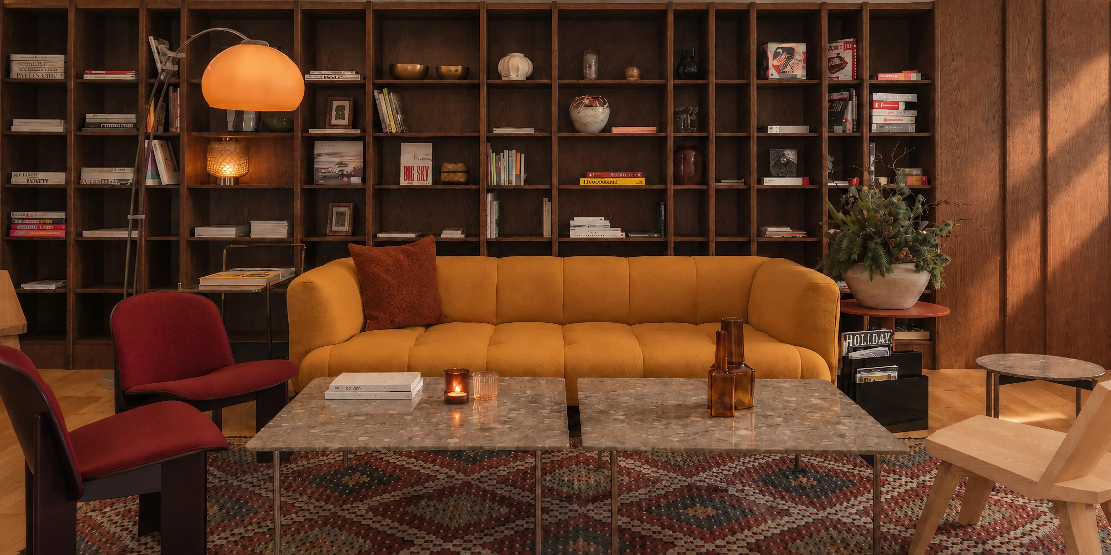 Hotellounge im La Senda Zuoz: dunkle Regalwand, ockerfarbenes Sofa, rote Sessel, Terrazzotische und Kelim-Teppich im Abendlicht